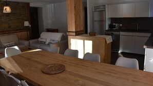 Eine moderne Küche mit weißen Schränken, einer Mikrowelle und einem Kühlschrank. Es gibt einen Holztisch mit Stühlen und eine Lampe, die von der Decke hängt.