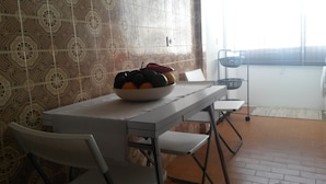Uma área de jantar com uma mesa posta para dois, uma tigela de fruta sobre a mesa e uma cadeira.