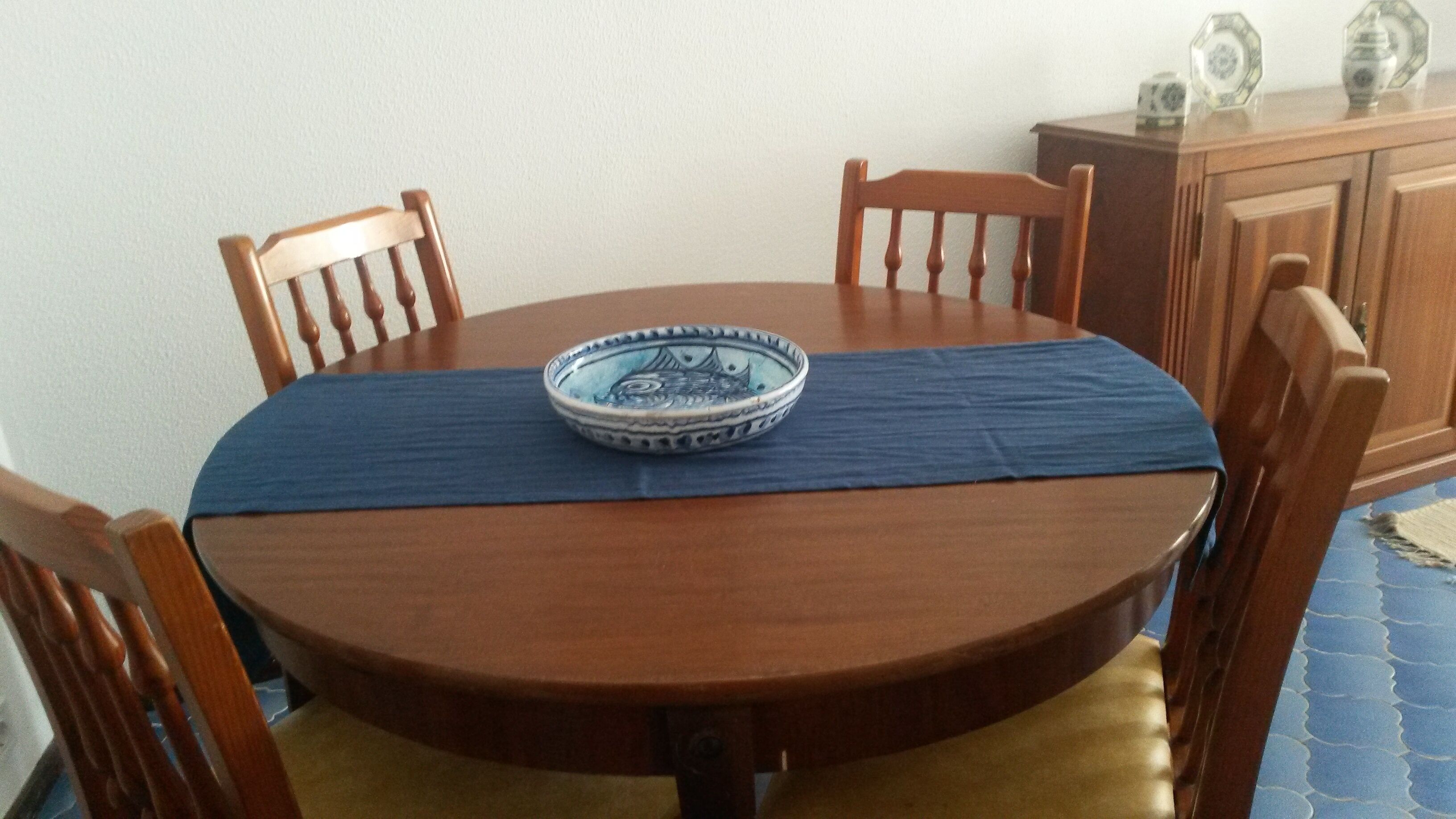Una taula de dinar rodona de fusta, coberta amb un teixit blau, i envoltada de cadires de fusta.