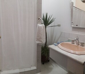A bathroom with a white bathtub, a sink, and a towel rack with a white towel. There is a potted plant next to the towel rack.