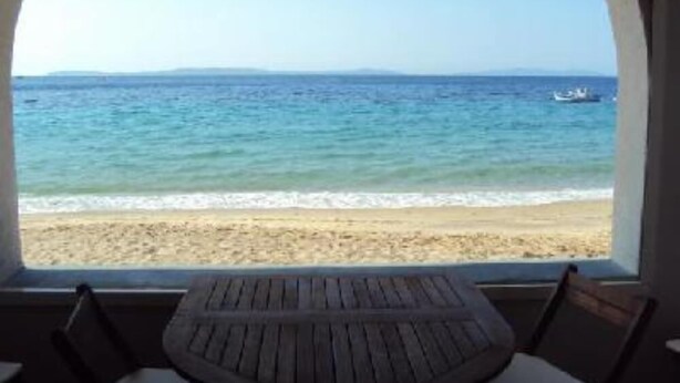 Uitzicht op het strand vanuit een kamer met een ronde houten tafel en twee stoelen.