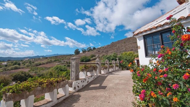 A building with a white facade, a balcony with a railing, and a view of a hilly landscape.