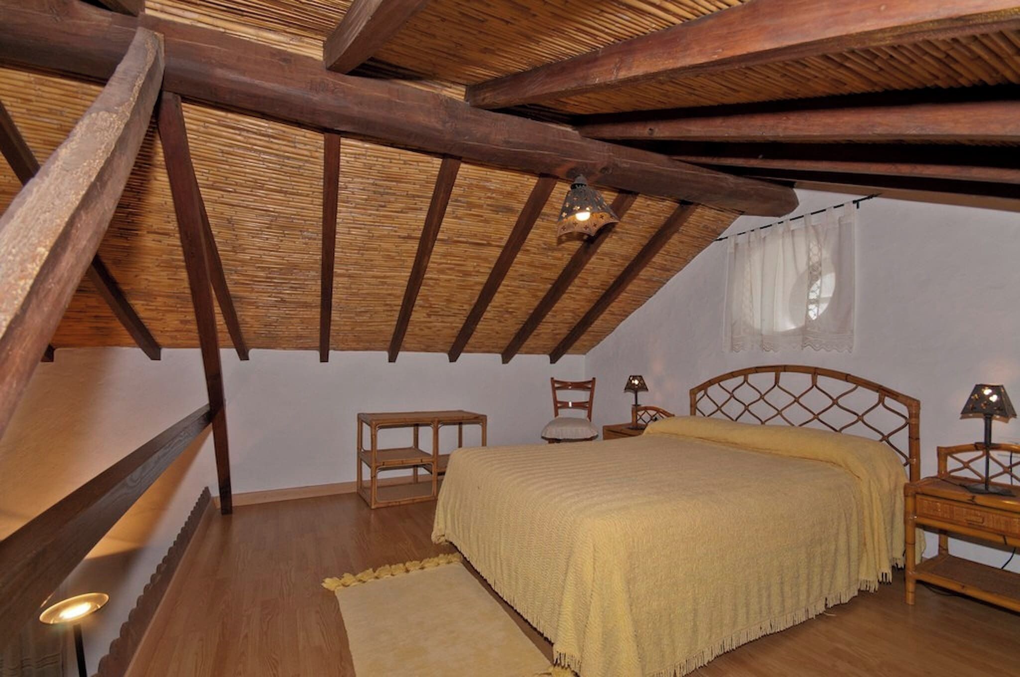Una camera da letto con soffitto in legno, un letto con coperta gialla, un comodino e una sedia.