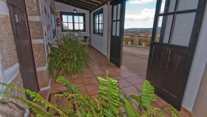 A covered patio area with a stone wall, a door leading outside, and a view of the countryside.