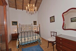A bedroom with a bed, a dresser, a chair, a nightstand, a chandelier, and two framed pictures on the wall. - GC0082 Holiday cottage in Teror (Teror)