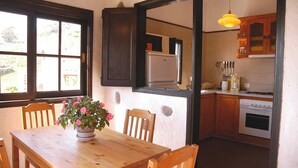 A dining area with a wooden table and chairs, a potted plant, and a view of a kitchen with wooden cabinets and appliances.