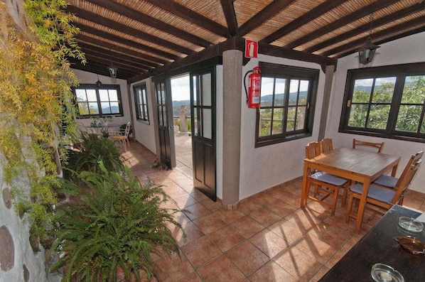 A covered patio with a table and chairs, a fire extinguisher, and a view of the outdoors. - GC0082 Holiday cottage in Teror (Teror)
