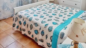 Een slaapkamer met een bed, een dressoir, een nachtkastje, een lamp en een raam met gordijnen.