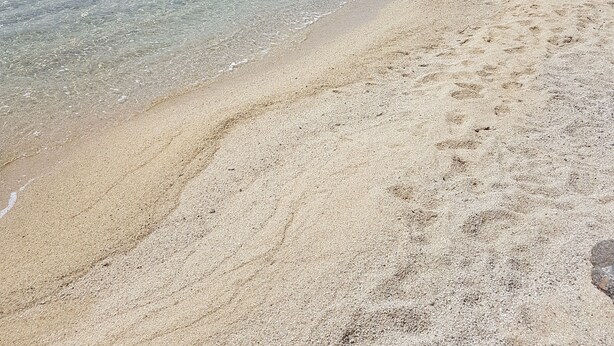 Een strand met helder water, een zandstrand en rotsformaties.
