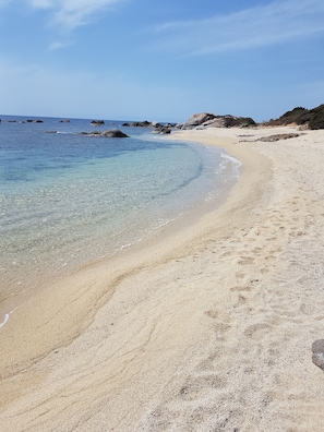 Una playa con agua cristalina, orilla de arena y afloramientos rocosos.