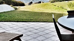 Een terras buiten met uitzicht op zee, een gazon en een betegelde vloer.