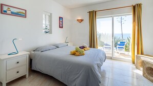 A bedroom with a bed, a nightstand, a lamp, and a view of the outside. - Apartment Isabel (Carvoeiro)