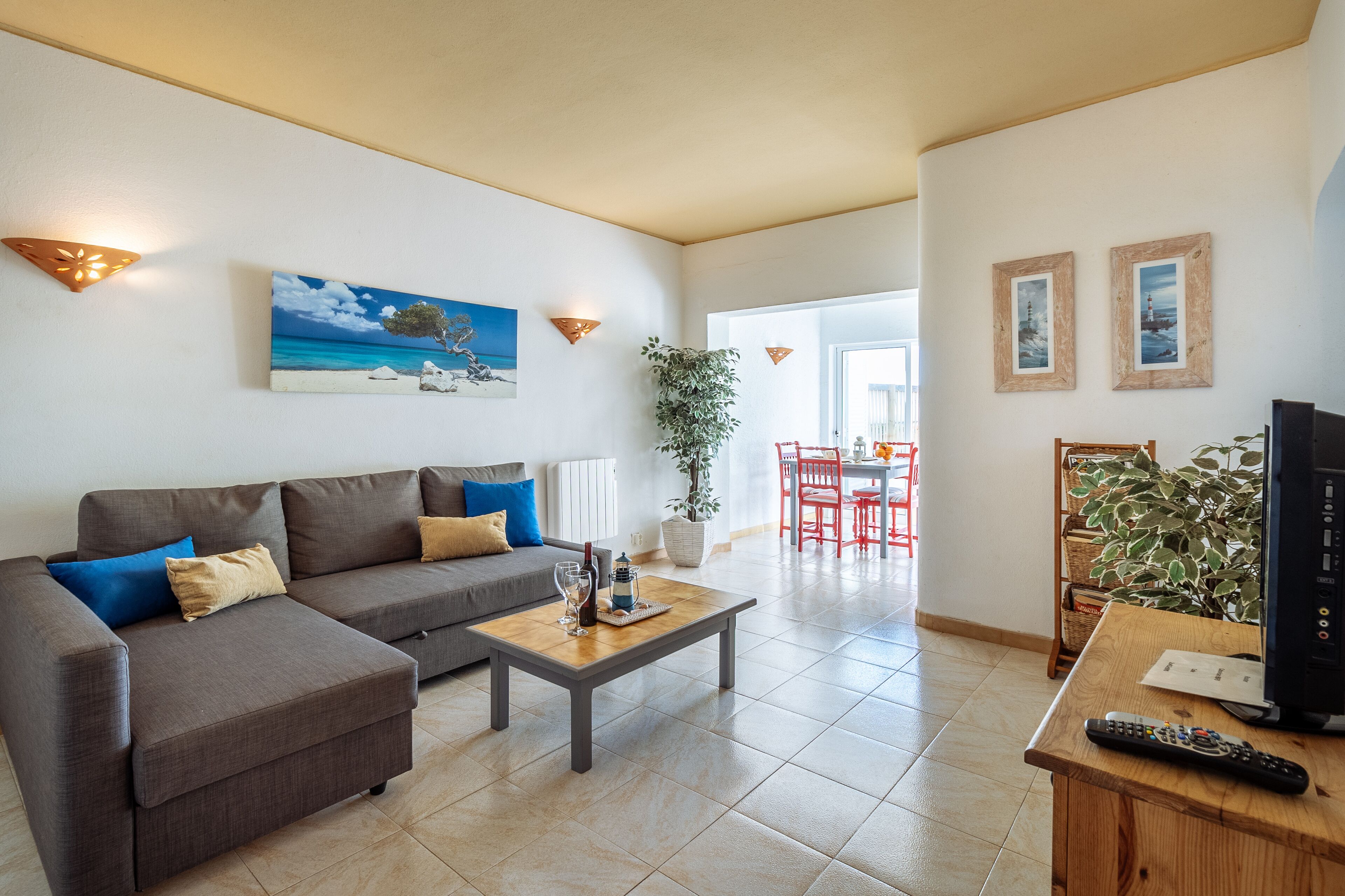 Un salon avec un canapé, une table basse et un meuble pour la télévision. Il y a un tableau au mur et une plante dans un coin.