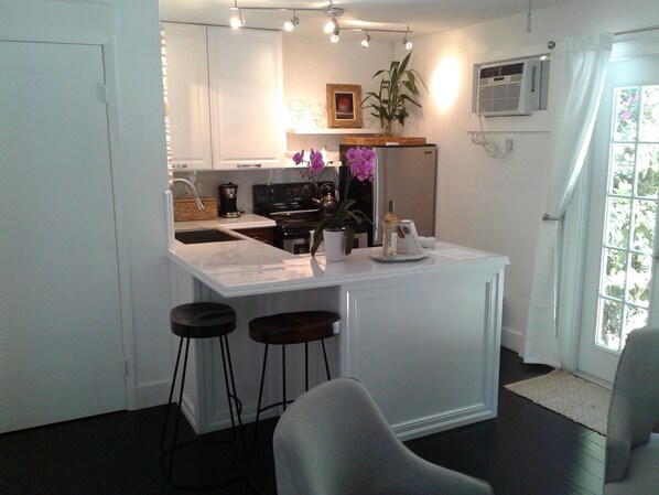 A modern kitchen with white cabinetry, a central island with bar stools, a refrigerator, and a potted plant.