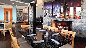 A restaurant with a stone wall, a fireplace, and cityscape artwork. Tables and chairs are neatly arranged. - Ocean Village Beach Condo, Golfcourse and Tennis Resort (Fort Pierce)