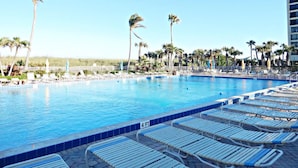 A swimming pool with lounge chairs, palm trees, and a clear sky. - Ocean Village Beach Condo, Golfcourse and Tennis Resort (Fort Pierce)