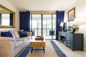 Relax in this inviting living room with a sofa, coffee table, and entertainment unit, featuring a large sliding glass door leading to a balcony with a view.