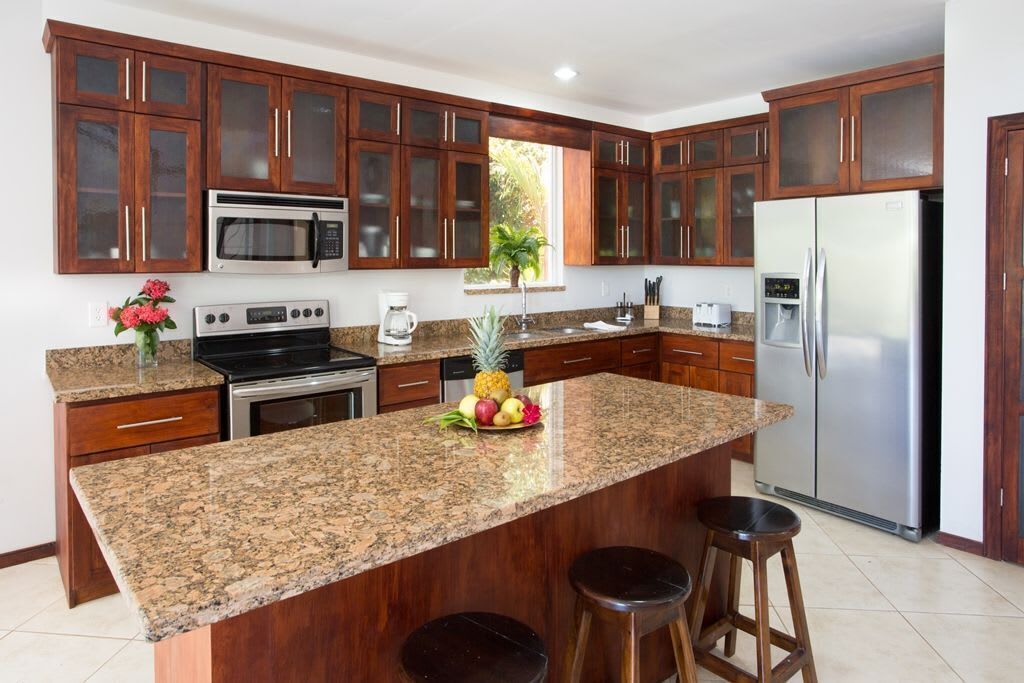 A kitchen with granite countertops, stainless steel appliances, wooden cabinets, and a central island with stools.
