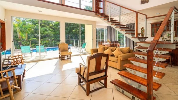 Un vaste espace de vie agrémenté d’un escalier en bois, de grandes fenêtres et d’une vue sur la piscine.