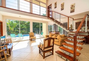 Un vaste espace de vie agrémenté d’un escalier en bois, de grandes fenêtres et d’une vue sur la piscine.