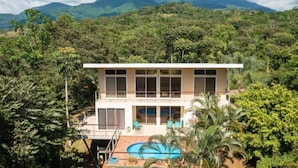 Un bâtiment moderne à deux étages, doté de grandes fenêtres, d’une piscine et entouré d’une végétation luxuriante.