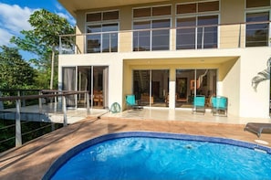 Un edificio de dos pisos con piscina, mobiliario exterior y un patio cubierto.