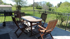 Eine Terrasse mit rundem Tisch, vier Stühlen, einem Sonnenschirm und einem Grill.