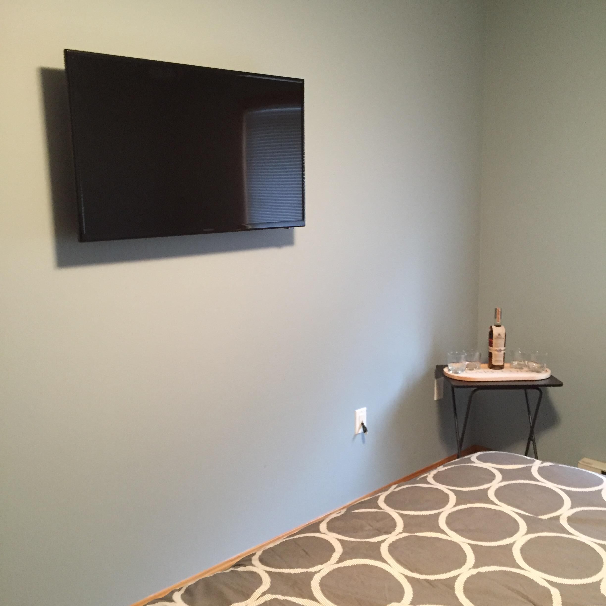 A room with a bed, a small table with a bottle and glasses, and a mounted TV.