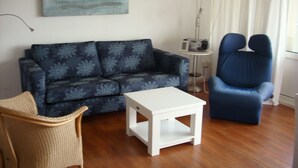 Una sala de estar con un sofá azul, una mesa de centro blanca, una silla de mimbre y un sillón azul.