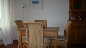 Un área de comedor con sillas de mimbre y una mesa de madera, una lámpara de pared y un reloj sobre un mueble de madera.