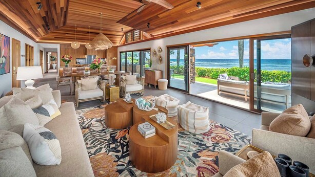A spacious living room with a large window overlooking the ocean, wooden ceiling, and a cozy seating area with a patterned rug. - Hale Luana By Parrish Kauai-beachfront estate with pool (Koloa)