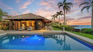 A poolside area with a house, outdoor furniture, and a view of the ocean at sunset. - Hale Luana By Parrish Kauai-beachfront estate with pool (Koloa)