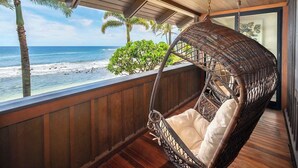 A wicker swing chair with a cushion on a wooden deck overlooking a beach. - Hale Luana By Parrish Kauai-beachfront estate with pool (Koloa)