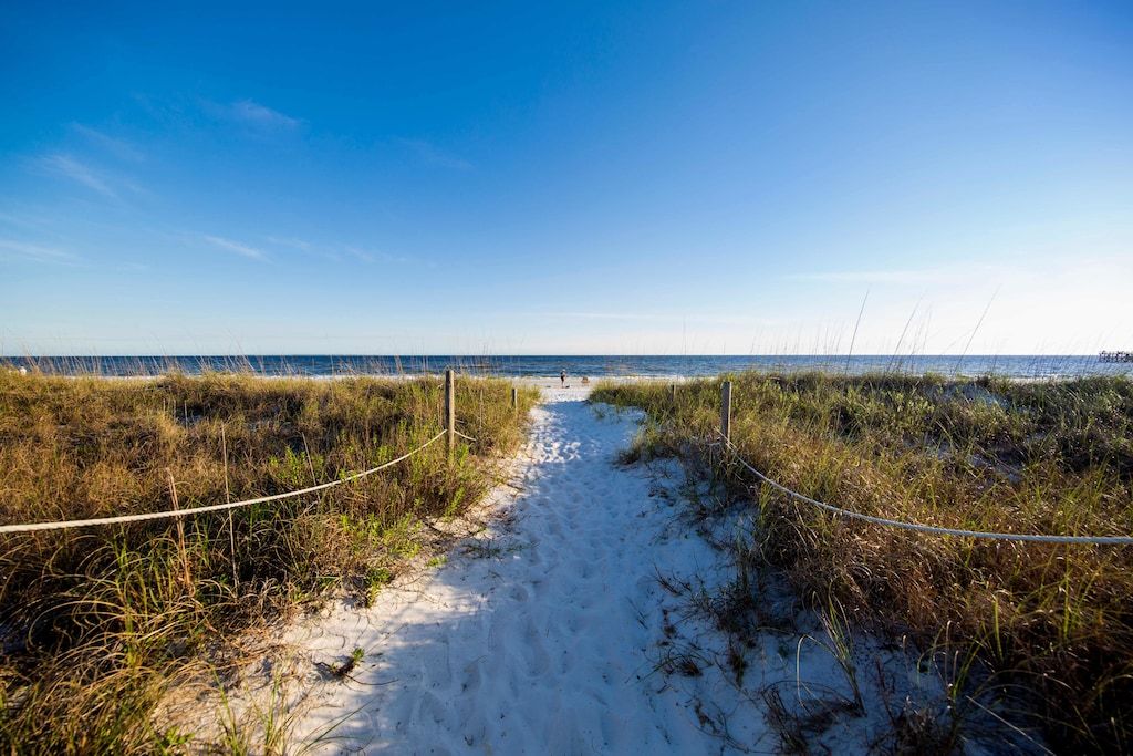 A sandy path leading to a beach with a clear sky.
