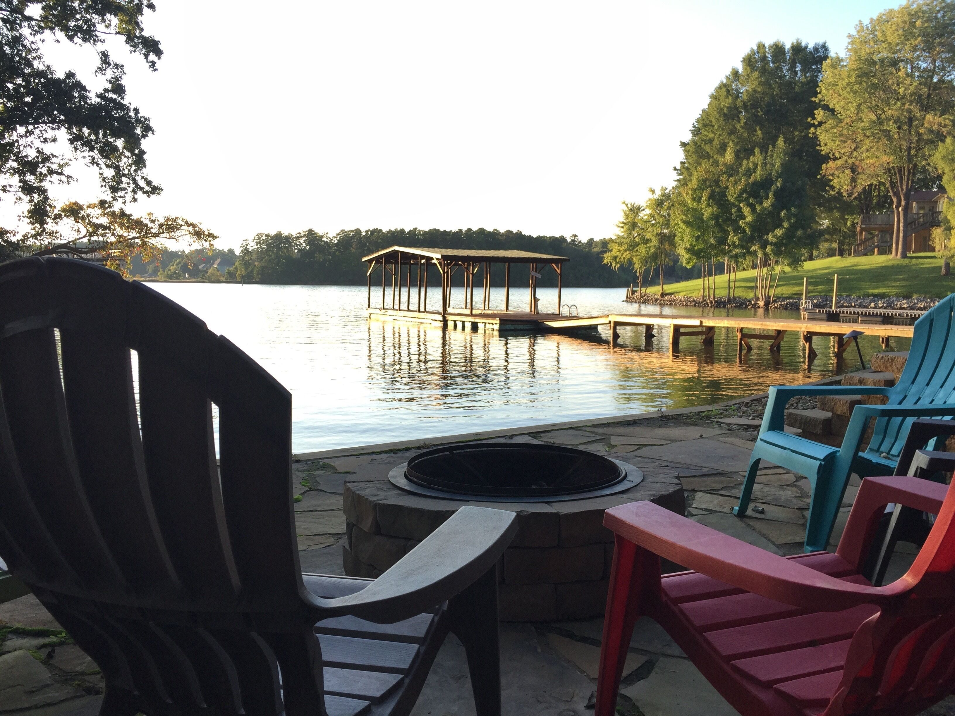 Un patio junto al lago con sillas Adirondack, un hogar para fuego y un muelle de madera que se adentra en el agua.