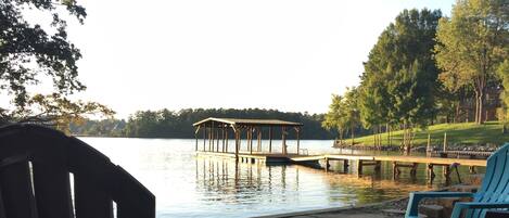 Un patio junto al lago con sillas Adirondack, un hogar para fuego y un muelle de madera que se adentra en el agua.