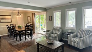 Un espace repas comprenant une table et des chaises en bois, une table basse et une vue sur l’extérieur grâce à une porte-fenêtre coulissante.