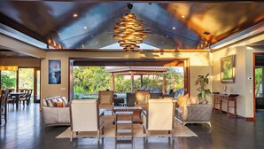 Un espace intérieur vaste et lumineux, doté d’un plafond au design moderne, d’un aménagement avec des canapés et des fauteuils, et offrant une vue sur l’extérieur.