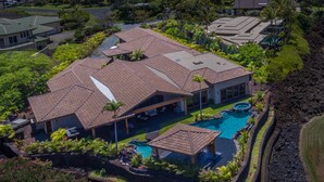 Une grande maison avec une piscine, entourée d’une végétation luxuriante et bordée d’une côte rocheuse.