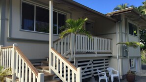 Ein zweistöckiges Haus mit einer Holztreppe, einem Balkon und einer kleinen Terrasse mit Stühlen und einem Blumentopf.