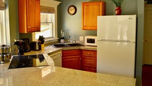 A kitchen with wooden cabinets, a white refrigerator, a microwave, an induction cooktop, and a sink.