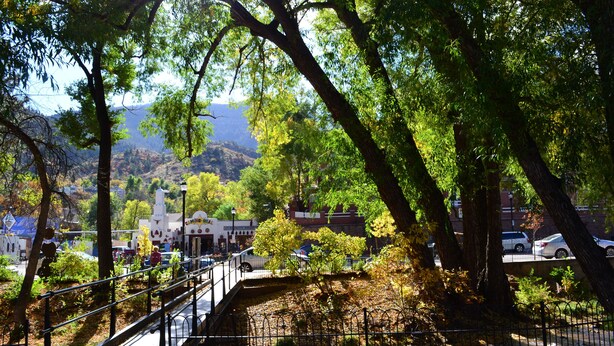 A park with a metal bridge, trees, and a distant view of buildings.