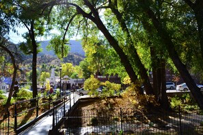 Un parque con un puente de metal, árboles y una vista distante de edificios.