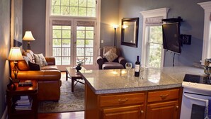 A kitchen with a granite countertop, wooden cabinets, and a built-in oven. There is a dining area with a brown leather couch and a side table with a lamp.