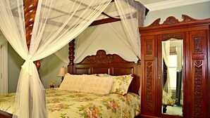 A bedroom with a four-poster bed, floral bedding, a wooden wardrobe, and a mirror.