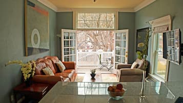 A spacious living room with a large window, a brown leather sofa, a glass coffee table, and a TV on the right.