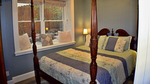 A bedroom with a four-poster bed, a window with a view of a wooden fence and greenery, and a bedside lamp. - The Heart of Manitou Springs. Award-winning. Luxurious. Historic. 1st Floor unit (Manitou Springs)