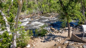 Un río con rocas y árboles, un sendero de tierra y un área cercada con una construcción.