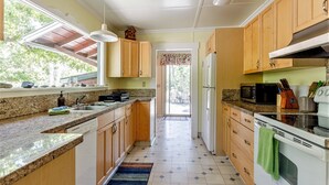 Una cocina con encimeras de granito, armarios de madera, lavavajillas, microondas y estufa.