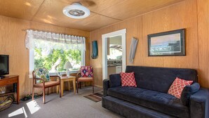 Un salón acogedor con un sofá oscuro, paredes de madera, un televisor y una ventana con cortinas.
